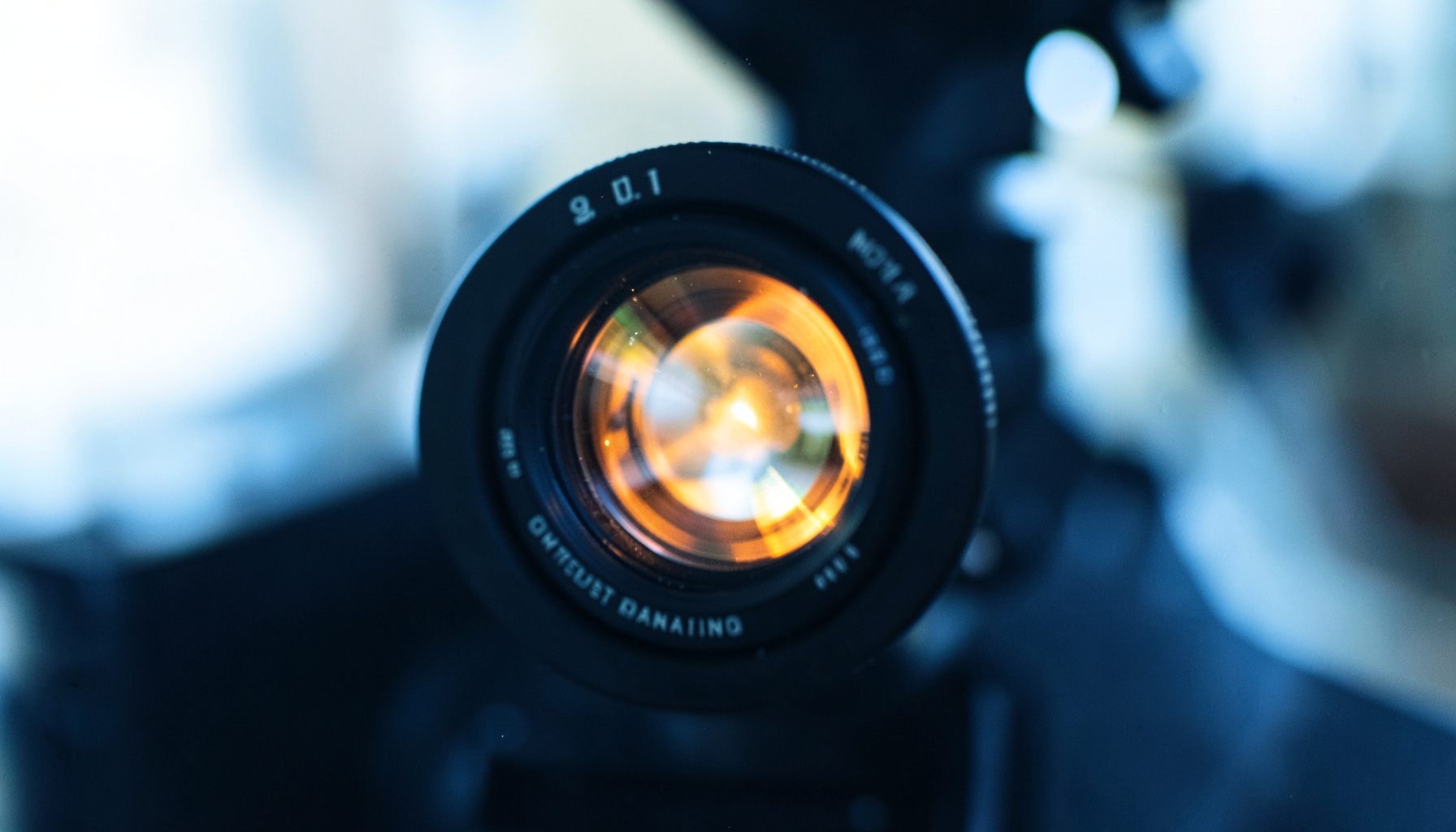 Close-up of a microscope lens catching warm amber light against a dark laboratory background